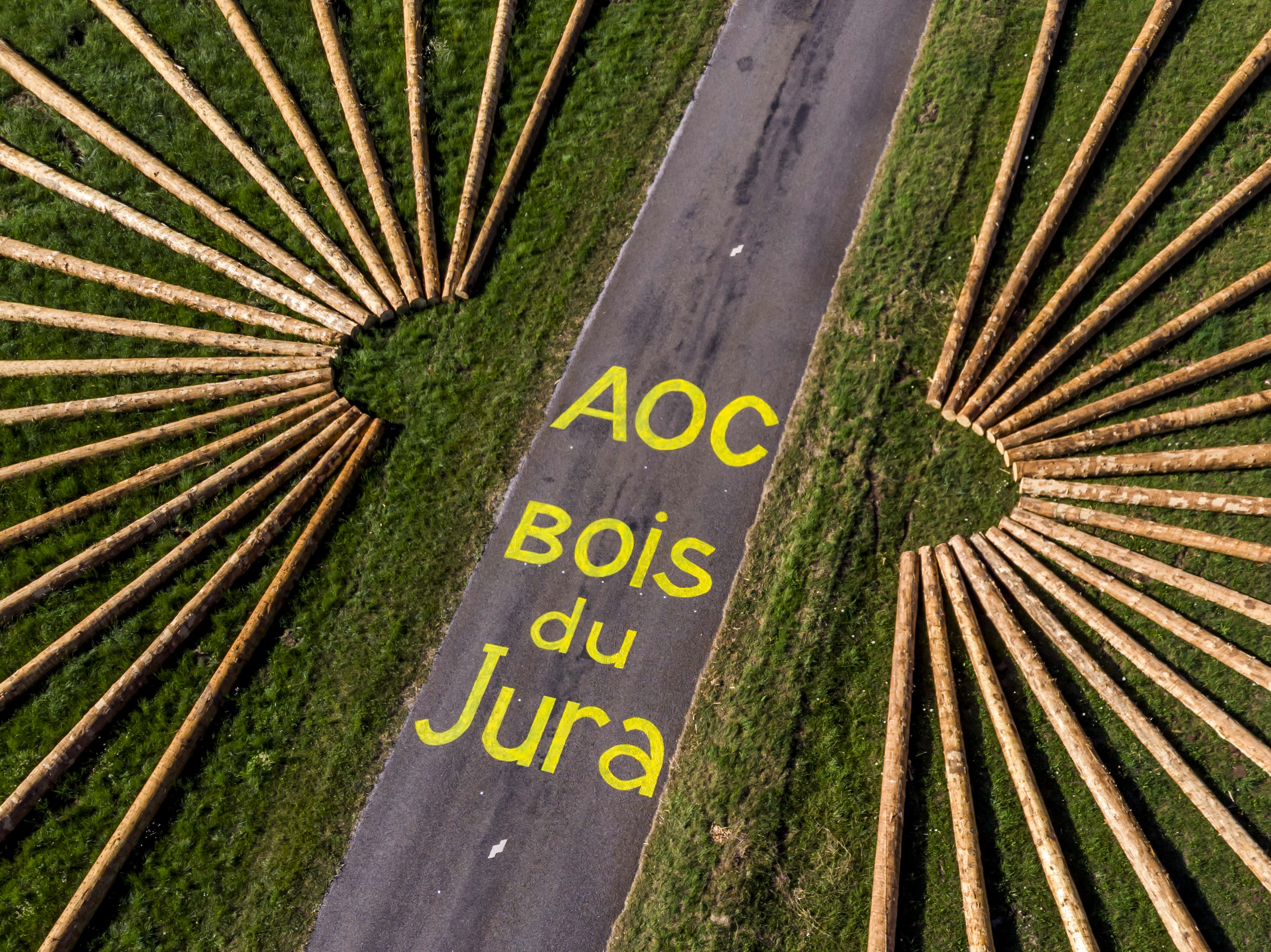 grumes de bois AOC disposées au sol formant un soleil ou des rayons de vélo. Sur la route au centre est inscrit "AOC Bois du Jura"